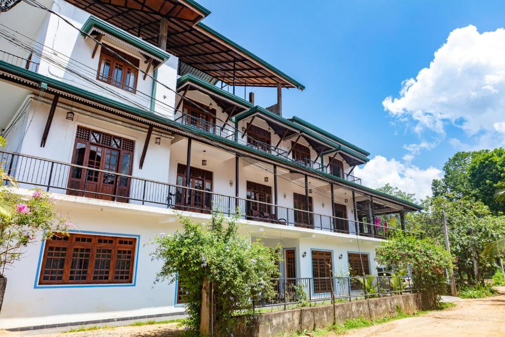 a large white building with balconies and trees at Shadow Inn Guest House in Ella