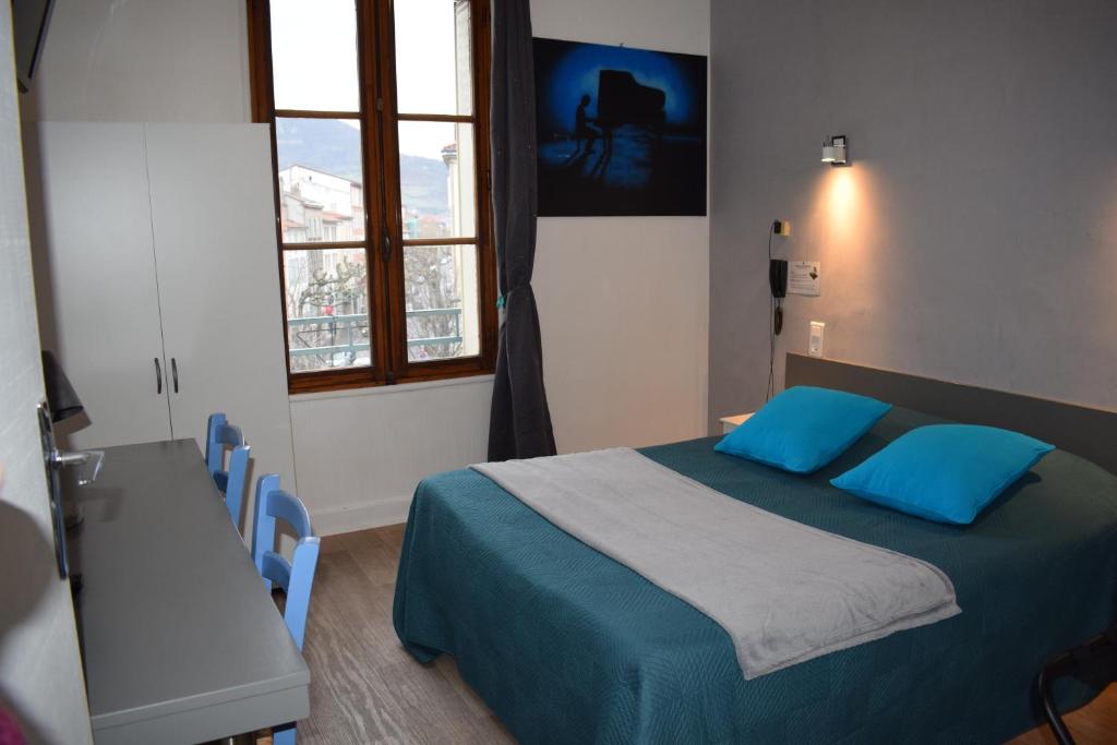 a bedroom with a bed with blue pillows and a window at Hôtel du Commerce in Millau
