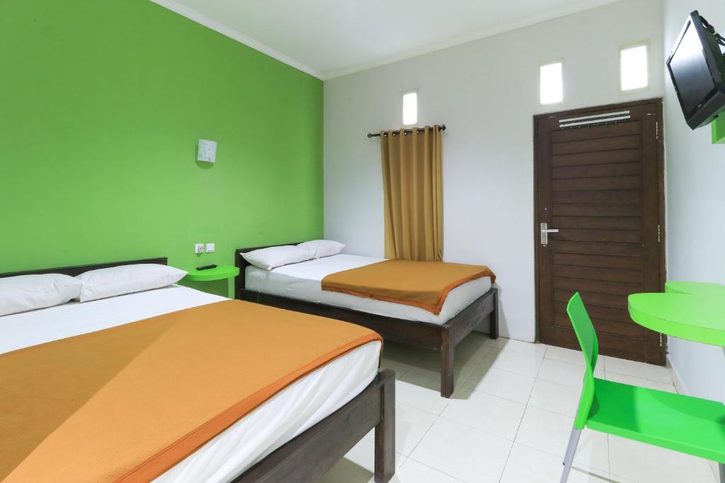 a green room with two beds and a table and a chair at Hotel Warta Putra in Denpasar