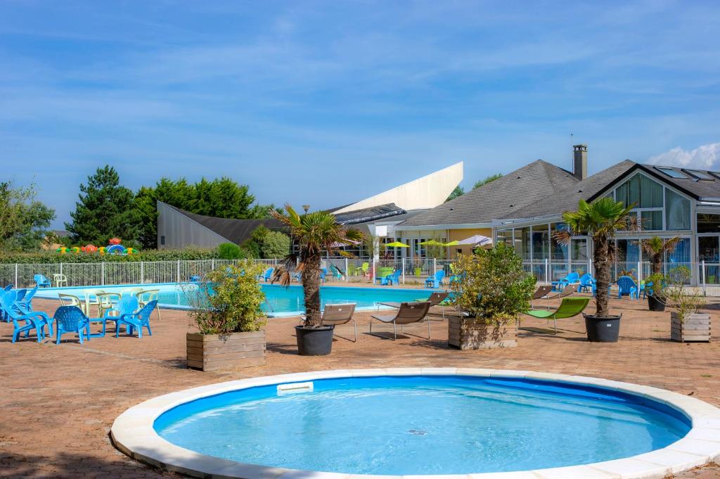 une piscine bordée de palmiers et de chaises ainsi qu'un bâtiment dans l'établissement VTF Le Sénéquet, à Blainville-sur-Mer