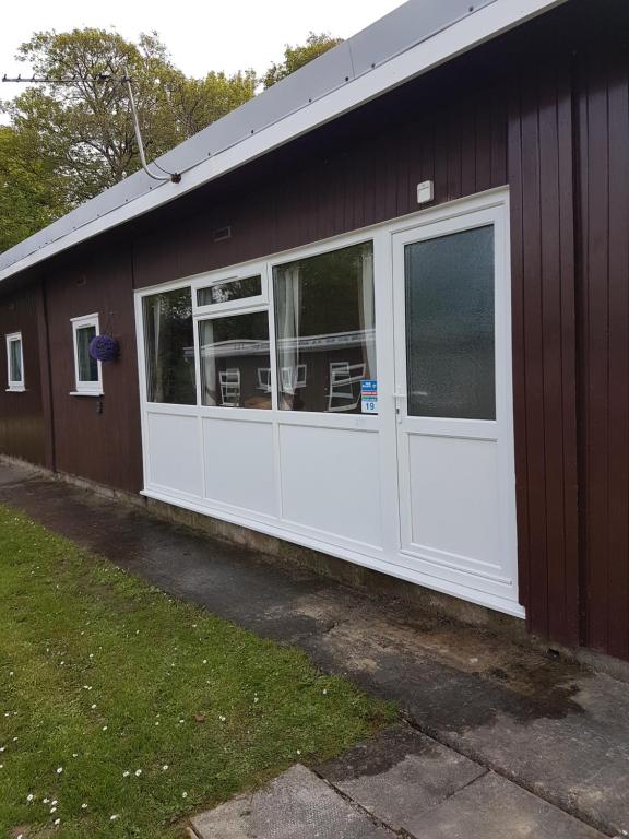 a brown building with a white door and windows at 19 Chalet Bucklands , Bideford Holiday Park. in Bucks Mills