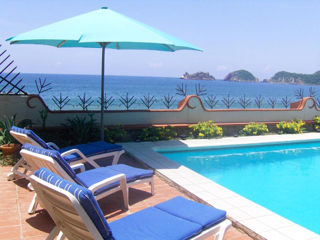 uma piscina com cadeiras e um guarda-sol e o oceano em La Paloma Oceanfront Retreat em San Patricio - Melaque