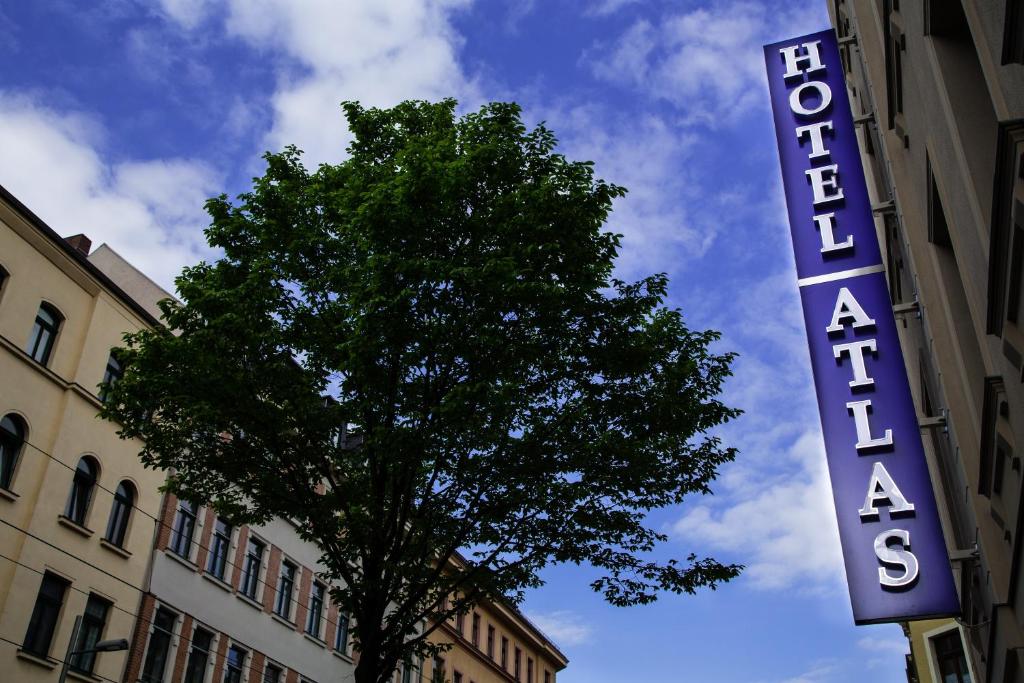 um sinal para um edifício com uma árvore em frente em Hotel Atlas Leipzig em Leipzig