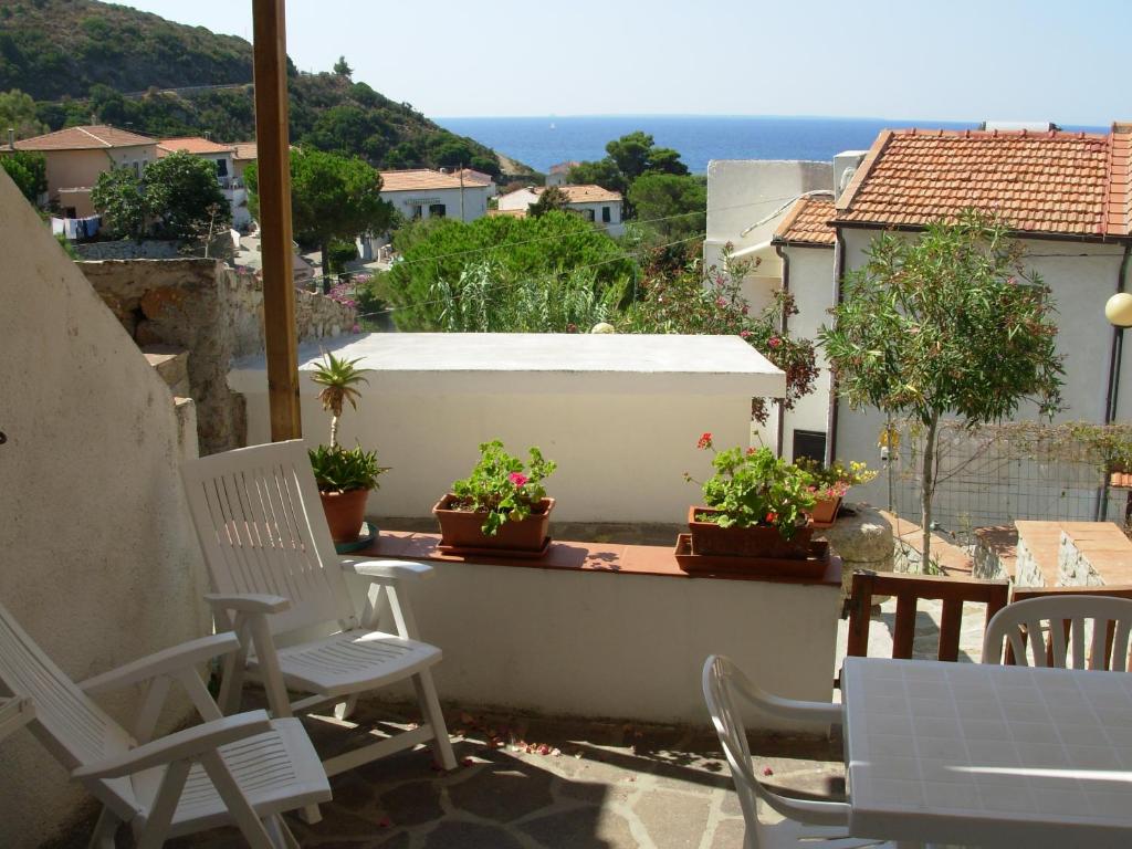 a patio with white chairs and potted plants on a balcony at Appartamento Il Nespolo in Pomonte