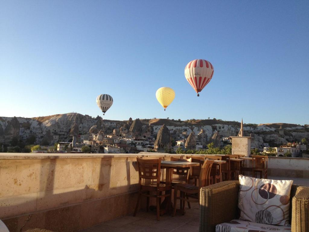 drei Heißluftballons fliegen über einen Balkon mit einem Tisch und Stühlen in der Unterkunft Walnut House in Goreme