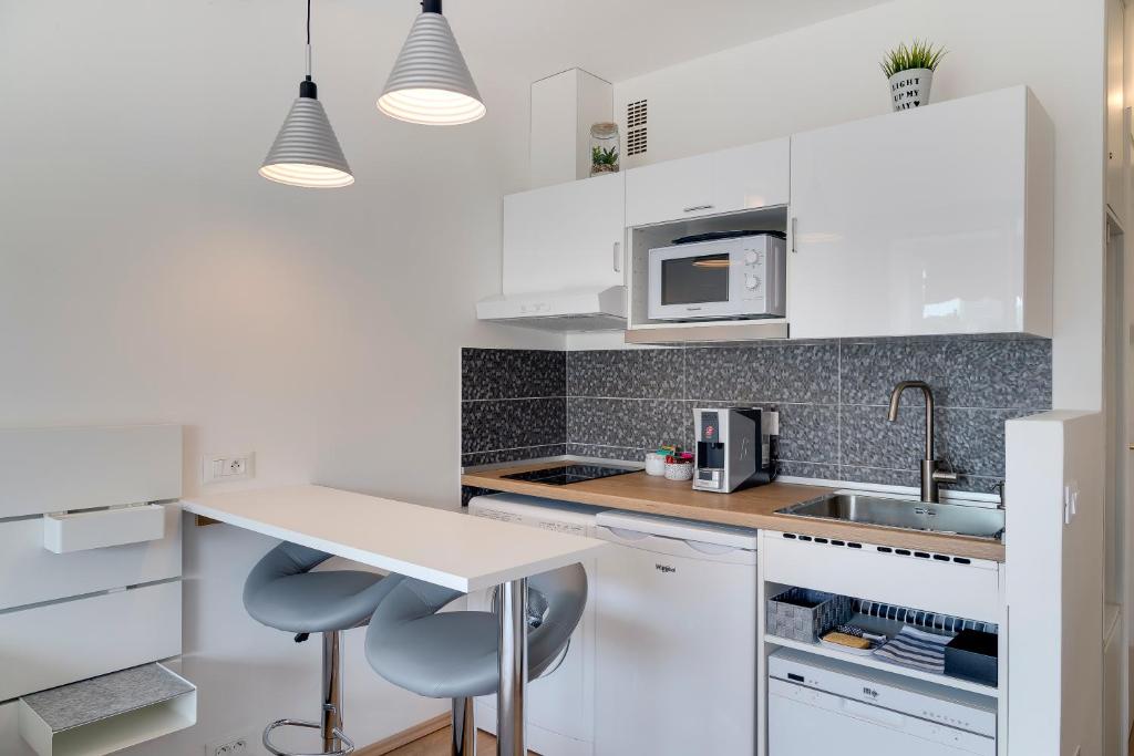a white kitchen with a sink and two stools at Studio la Plage in Roquebrune-Cap-Martin