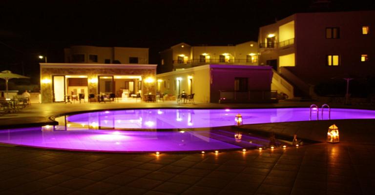 una piscina iluminada en púrpura por la noche en Sandy Suites en Kalamaki Chanion