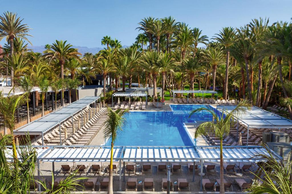 
a beach with a pool, chairs, and a balcony at Hotel Riu Palace Oasis in Maspalomas
