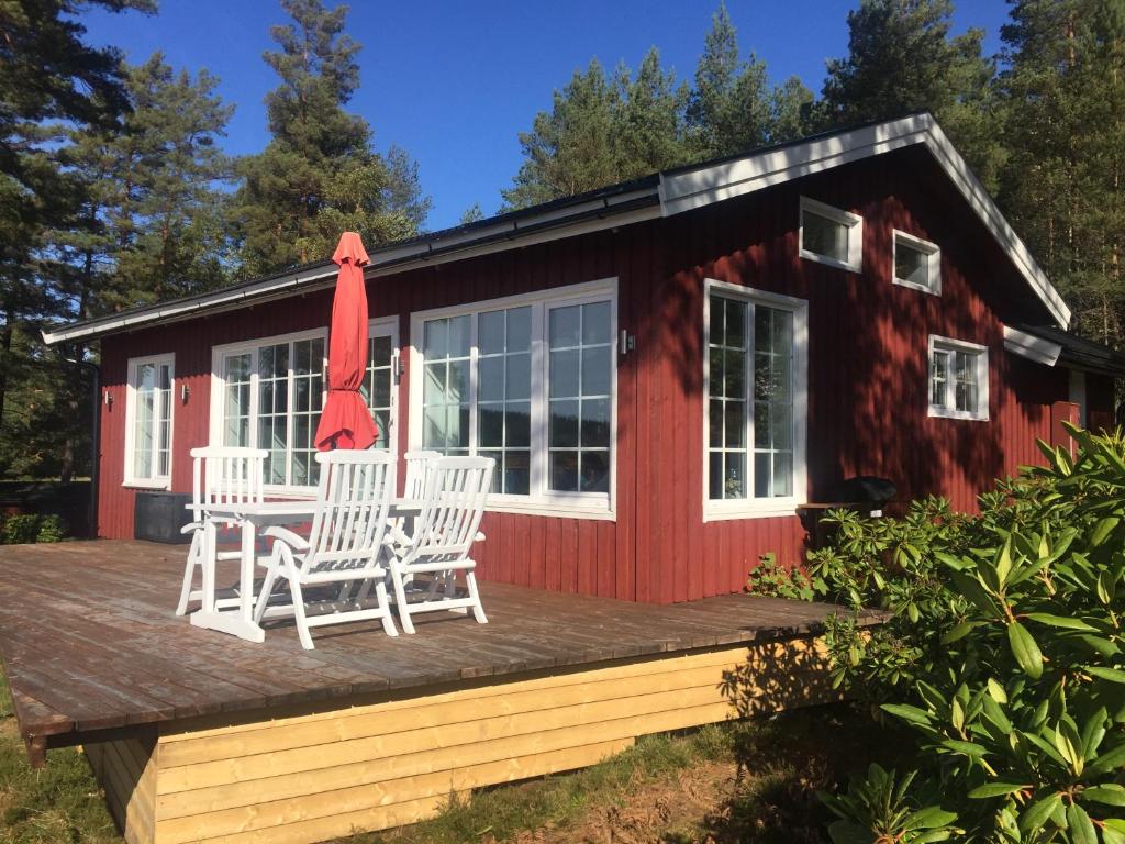 a red cabin with two chairs and an umbrella on a deck at Haus Kilstrand in Tämta