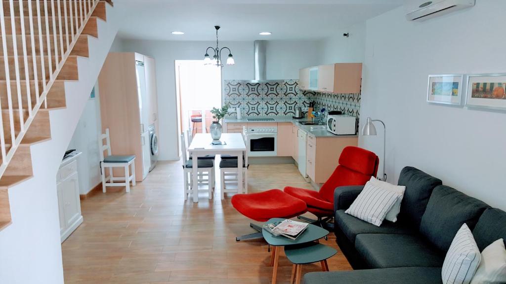 a living room with a couch and red chairs and a kitchen at Adosado en playa de la Barrosa, casa Carlota in Chiclana de la Frontera