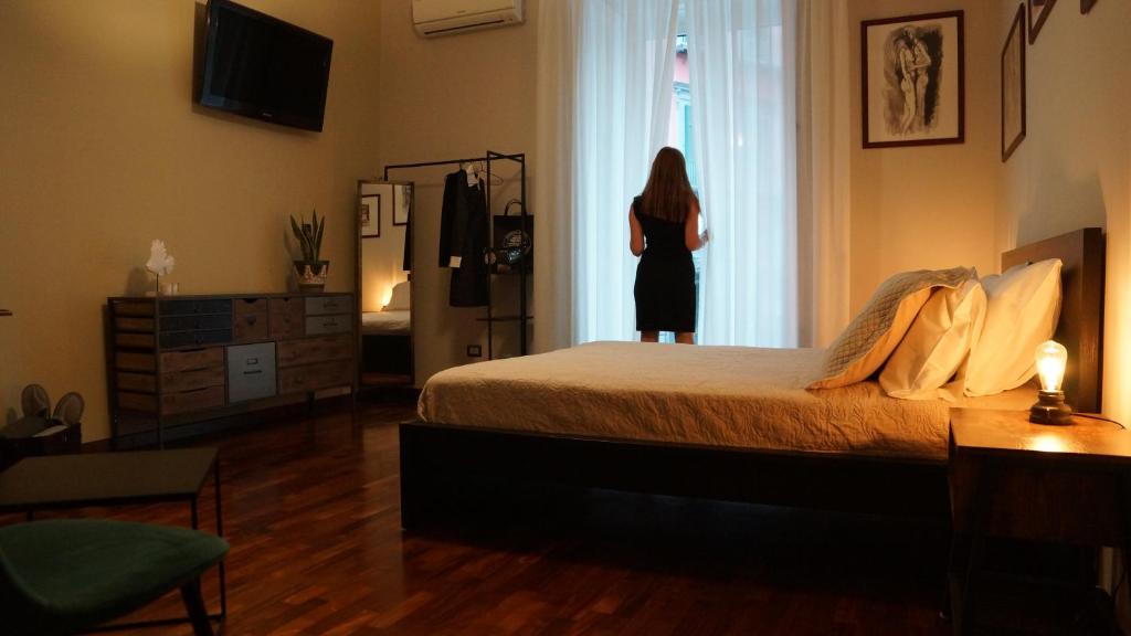 Eine Frau, die in einem Schlafzimmer steht und aus dem Fenster schaut. in der Unterkunft Finest apartment - nel cuore di Napoli in Neapel