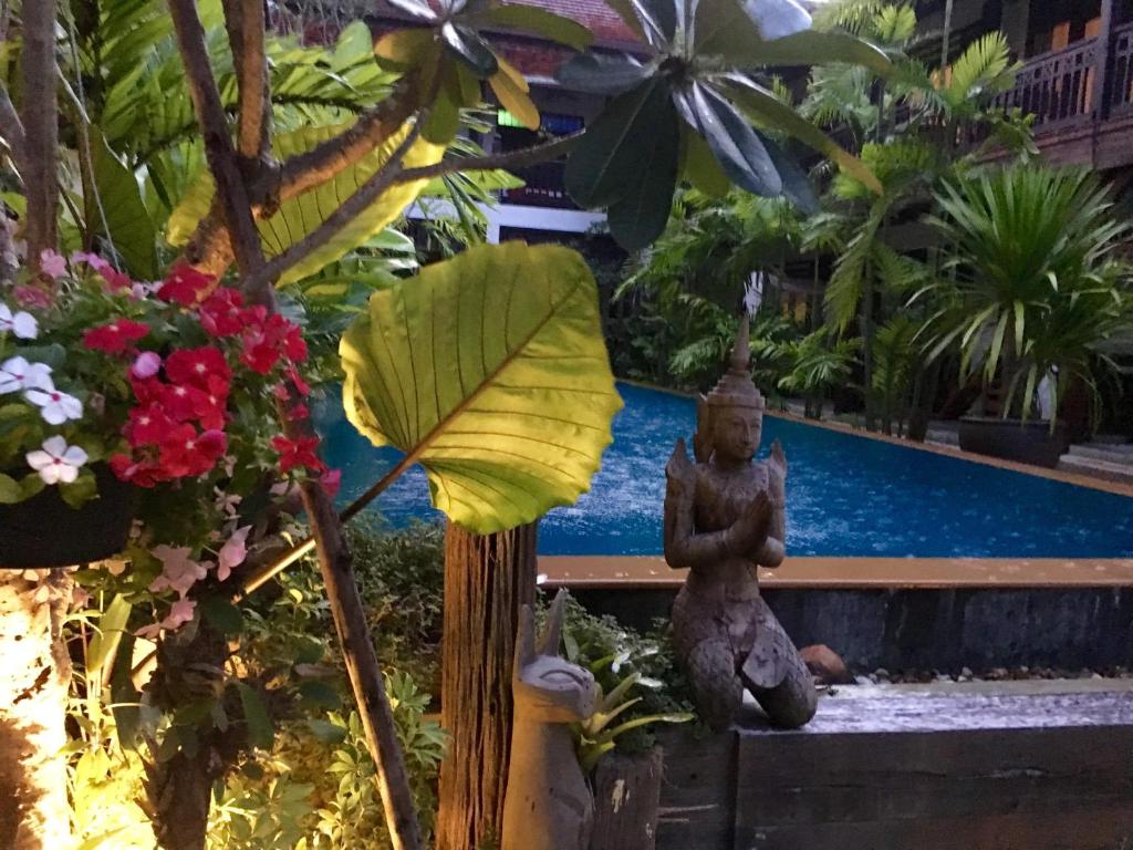 A warmly lit poolside garden with a seated statue and tropical flowers.