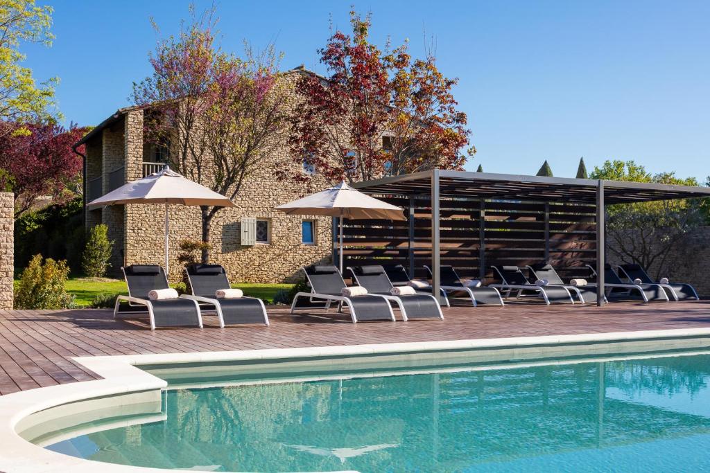 una piscina con sedie a sdraio e ombrelloni di Hôtel Carcarille Restaurant Le C a Gordes