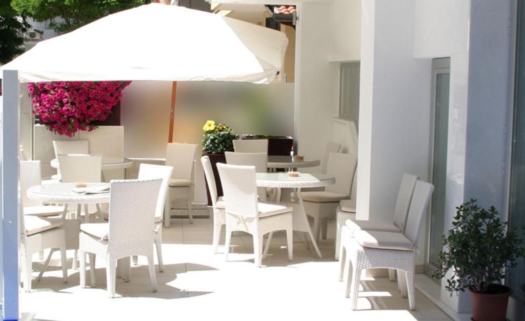 un patio con tavoli e sedie bianchi e ombrellone di Hotel Loretta a Rimini