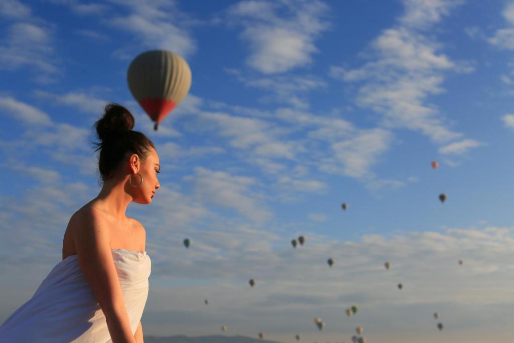 Uma mulher num vestido branco a olhar para um balão de ar quente. em Mirzade Konak Hotel em Goreme