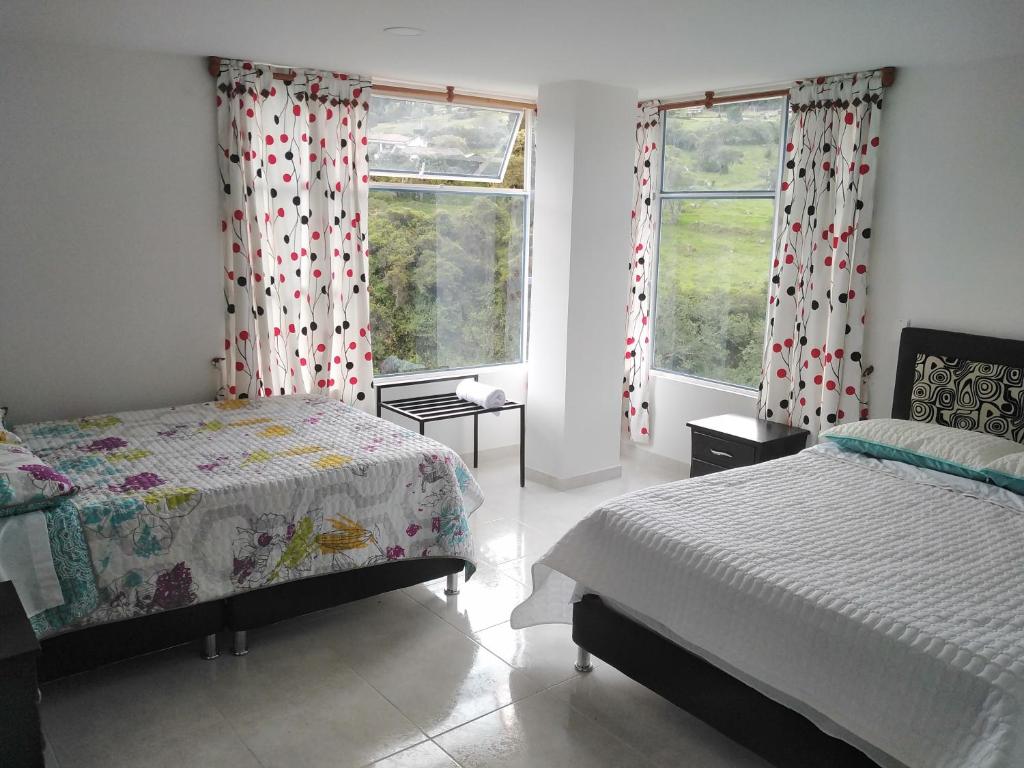 een slaapkamer met 2 bedden en 2 ramen bij Hotel Alta Montaña in Tópaga