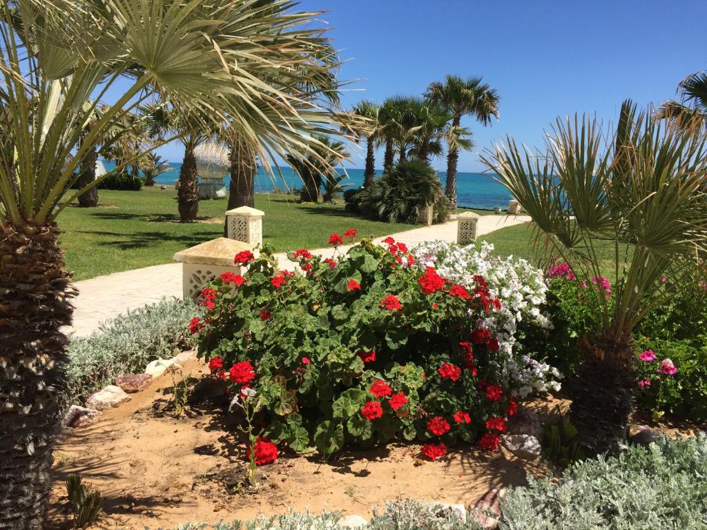 a garden with red and white flowers and palm trees at La mer carrément à vos pieds in Hammamet