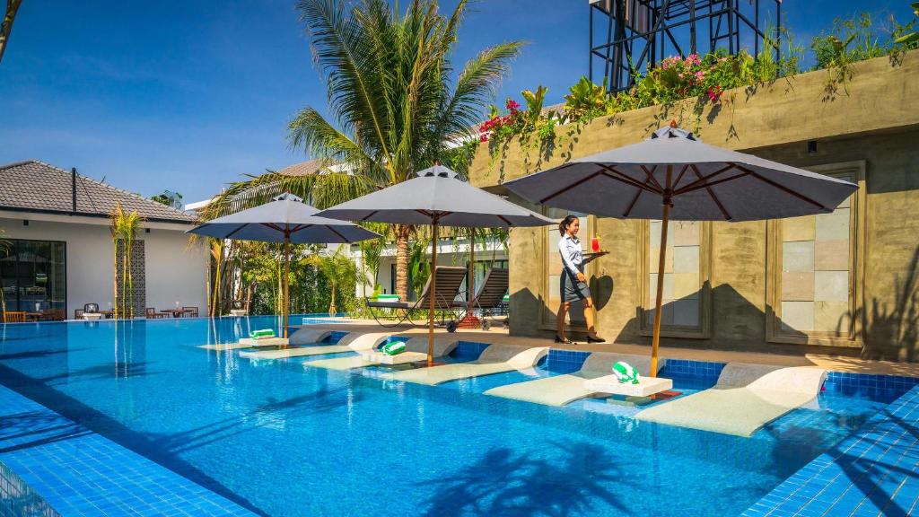 a woman standing next to a swimming pool with umbrellas at Grand Venus La Residence in Siem Reap
