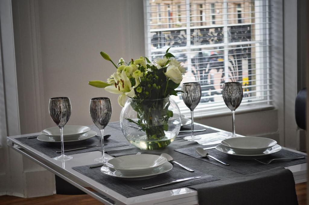 a table with plates and glasses and a vase of flowers at Apartment 4 Hamilton Square in Birkenhead