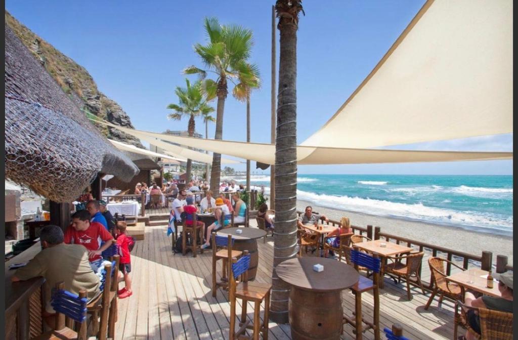 Apartamentos Torreon Del Mar في بينالمادينا: مجموعة من الناس يجلسون على الطاولات على الشاطئ