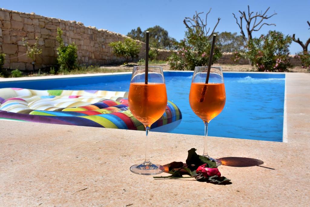 dos copas de champán sentadas en una mesa junto a una piscina en Four Winds Farmhouse, en Birżebbuġa