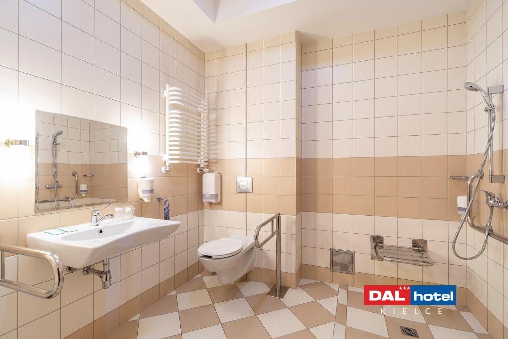 Tiled accessible restroom featuring sink, raised toilet, grab rails, handheld shower and soap dispensers.