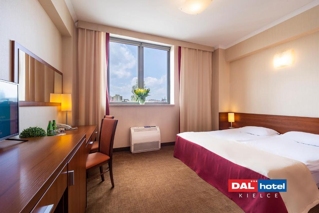 Hotel room with double bed, wooden desk, window with vase of flowers, warm neutral decor.