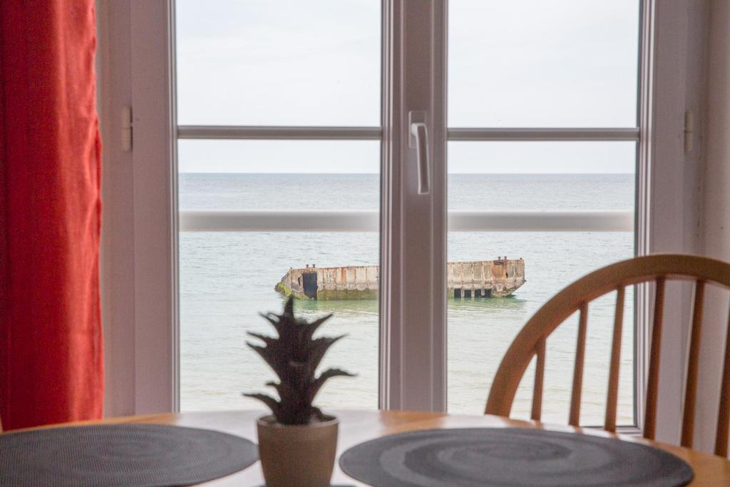 a table with a view of the ocean from a window at Appartement sur la Plage 4 Personnes in Arromanches-les-Bains