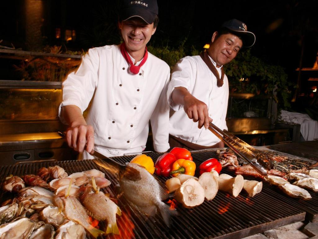 two men cooking on a grill with meat and vegetables at Caesar Park Hotel Kenting in Kenting