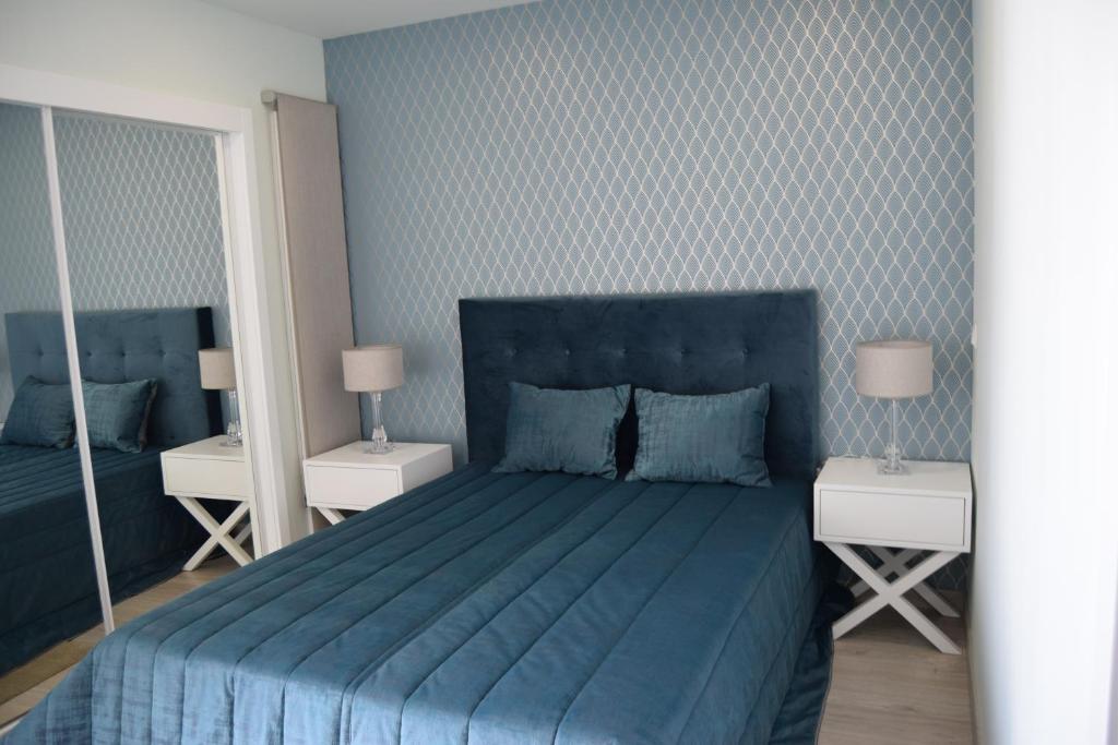 1 dormitorio con 1 cama azul, 2 mesas y 2 espejos en magnifico apartamento, en Albufeira