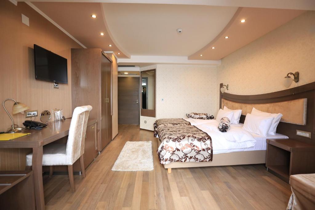 Hotel room with double bed, patterned runner, wall-mounted TV, work desk with chair, bedside lamps and wood flooring at City Palace Hotel in Ohrid