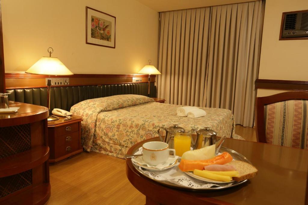 a hotel room with a bed and a tray of food on a table at Hotel Gran Corona in Sao Paulo