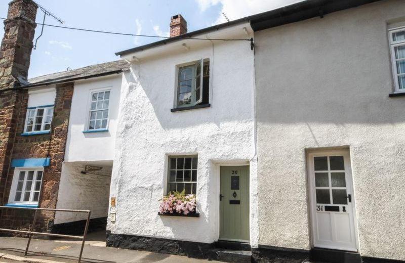 a white house with a green door and flowers in a window at Inglenook Cottage in Crediton