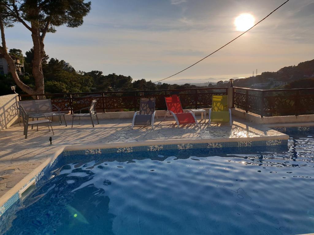 a swimming pool with chairs and a table and the sun at Studio d'environ 20m2, piscine, vue mer, pour 2 personnes in Marseille