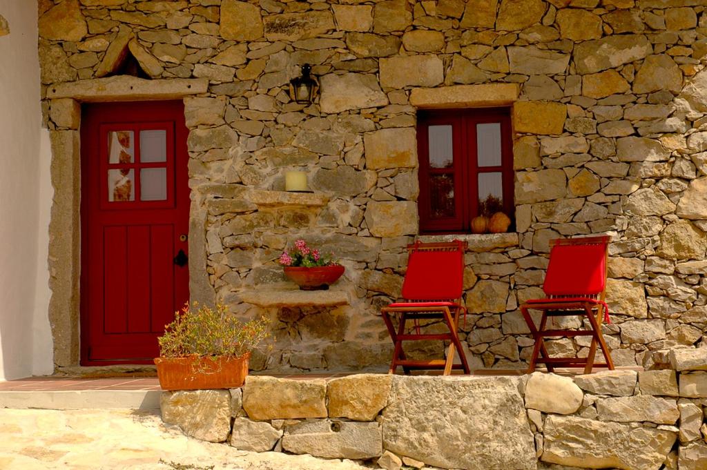 a stone building with two red doors and two chairs at Casal da Serrana in Reguengo Grande