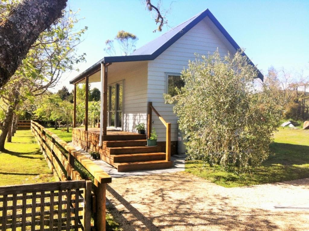 una pequeña casa blanca con una valla de madera en Mirror Creek Holiday Cottage en Ruatapu