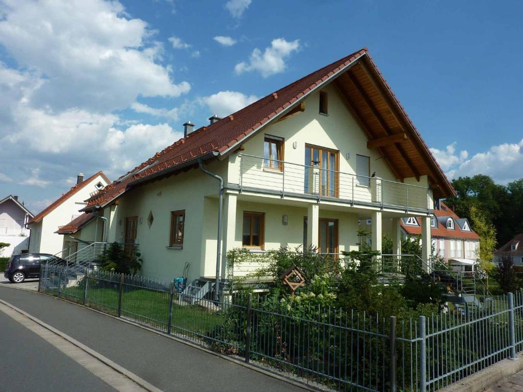 a white house with a brown roof and a fence at Ferienwohnung Fantaisie in Eckersdorf