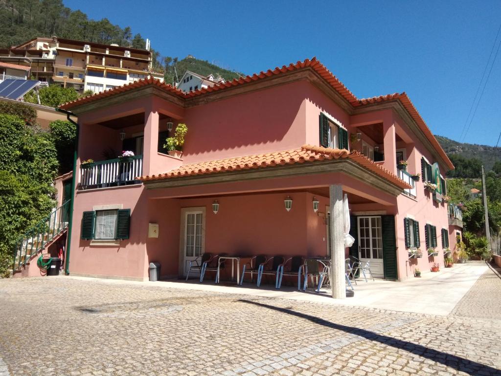 ein rosafarbenes Haus mit Tischen und Stühlen davor in der Unterkunft Residencial Ribeiro in Geres