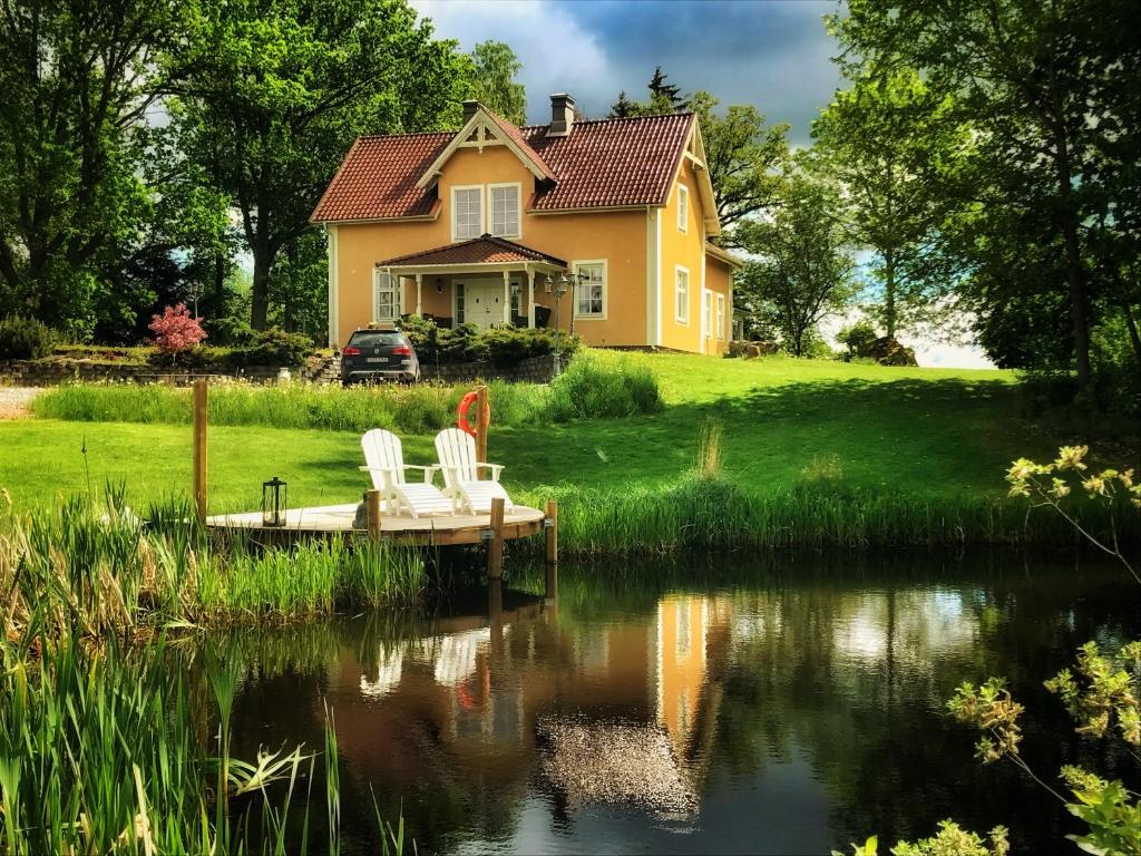 ein gelbes Haus mit zwei Stühlen auf einem Dock neben einem See in der Unterkunft Hidingsta gård B&B in Örebro