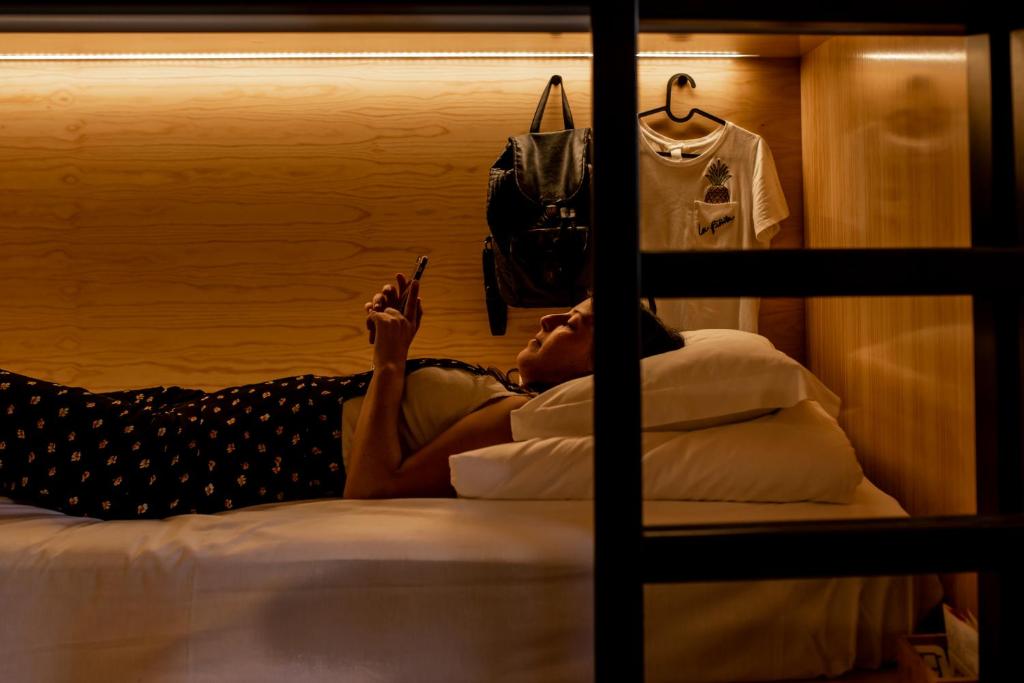 a woman laying on a bed next to a bunk bed at GiG Capsule Hostel in Ericeira