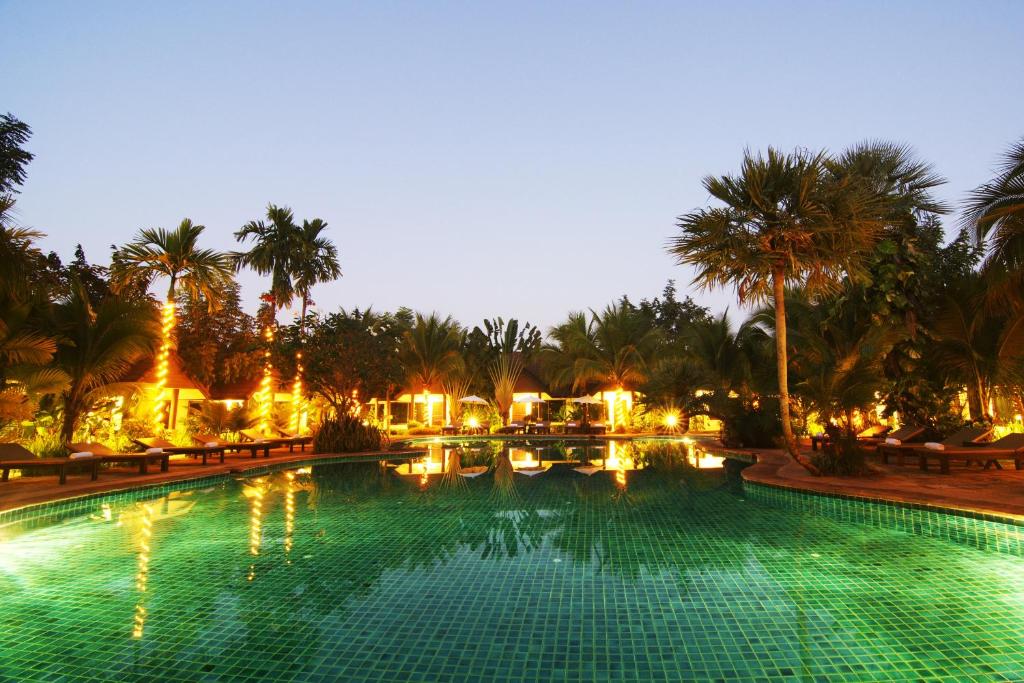 a large swimming pool with palm trees at night at Laluna Hotel And Resort, Chiang Rai in Chiang Rai