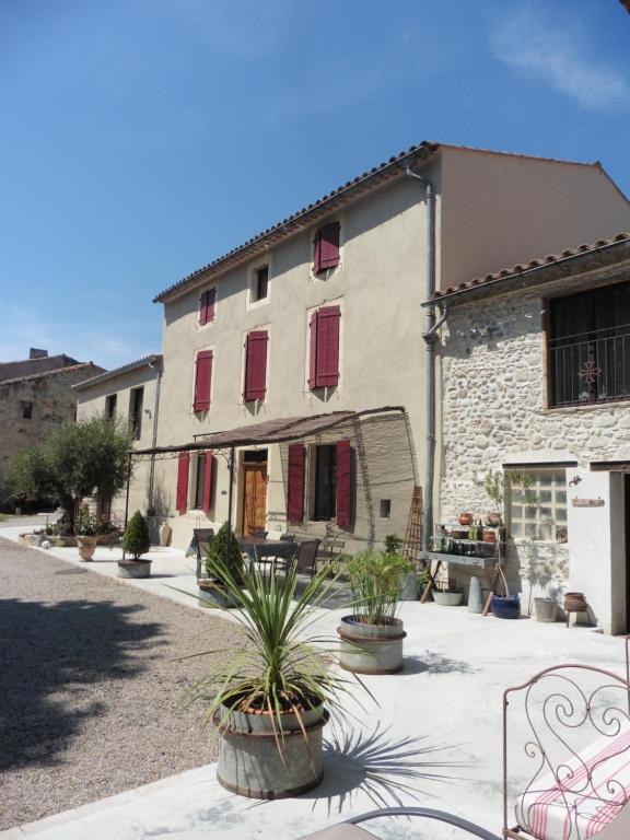 a building with red shuttered windows and plants in a courtyard at L'Albane Chambres d'hôtes in Lauraguel