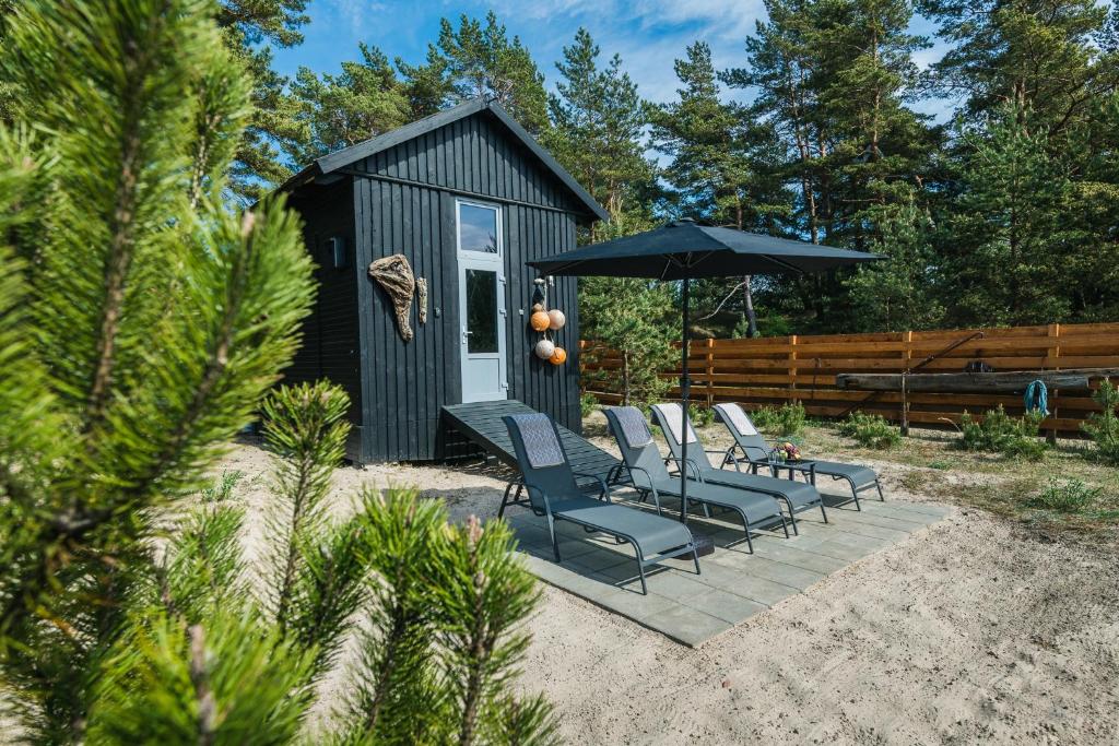 a black tiny house with chairs and an umbrella at Jūras Krasti Bohemija in Jūrmalciems
