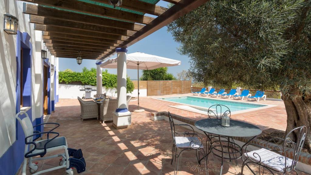 a patio with a table and an umbrella and a pool at Casinhas Wheelchair friendly in Boliqueime