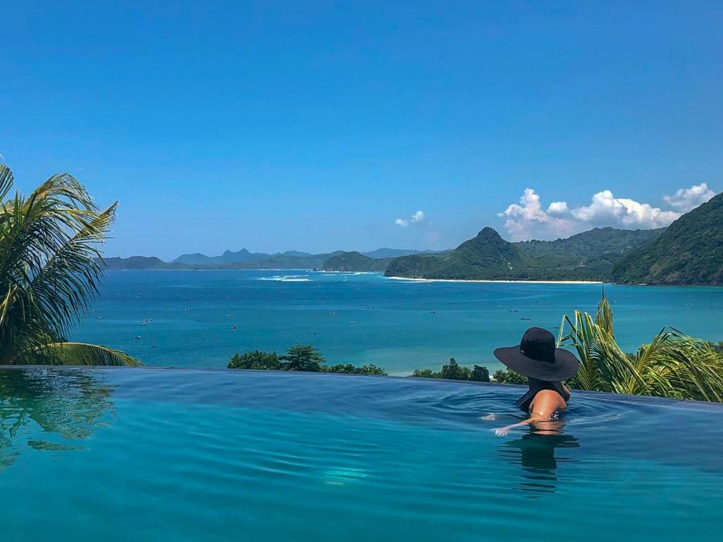 a person in a hat sitting in a pool overlooking the ocean at Sempiak Seaside Resort in Selong Belanak