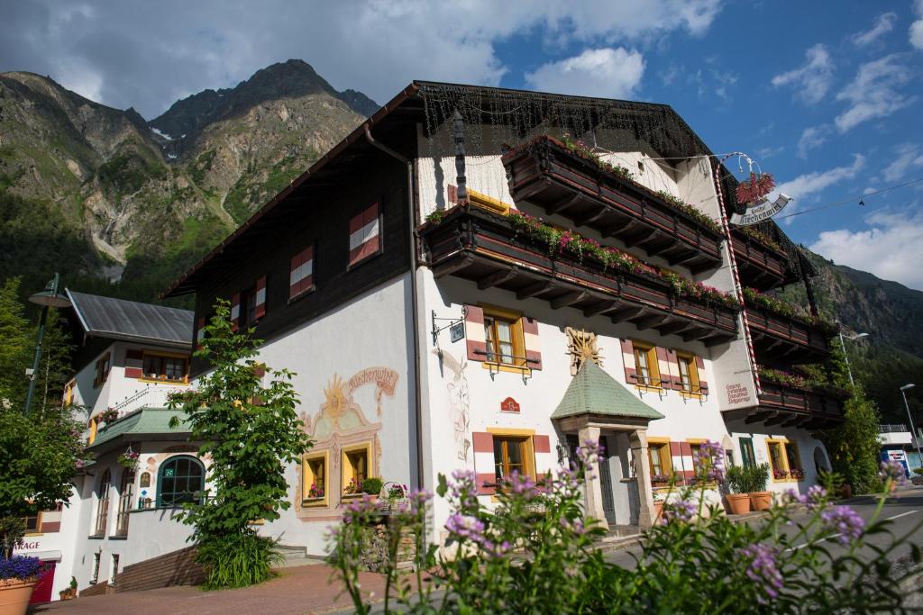 a building with flowers in front of a mountain at Hotel Garni Kirchenwirt in Sankt Leonhard im Pitztal