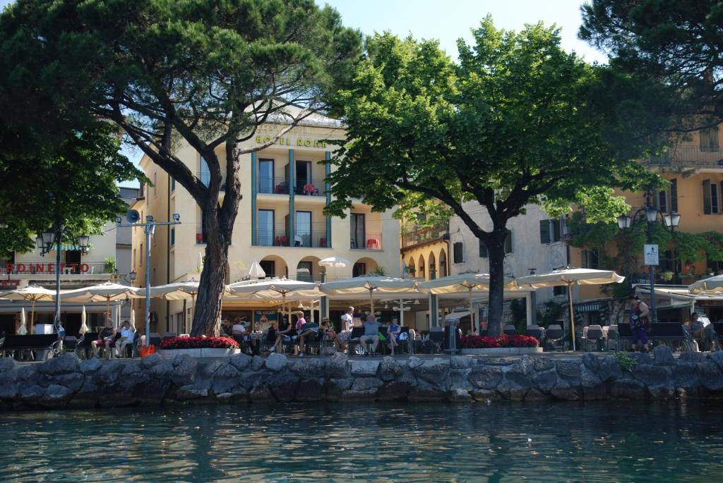 a group of tables and umbrellas next to a body of water at Hotel Roma in Garda