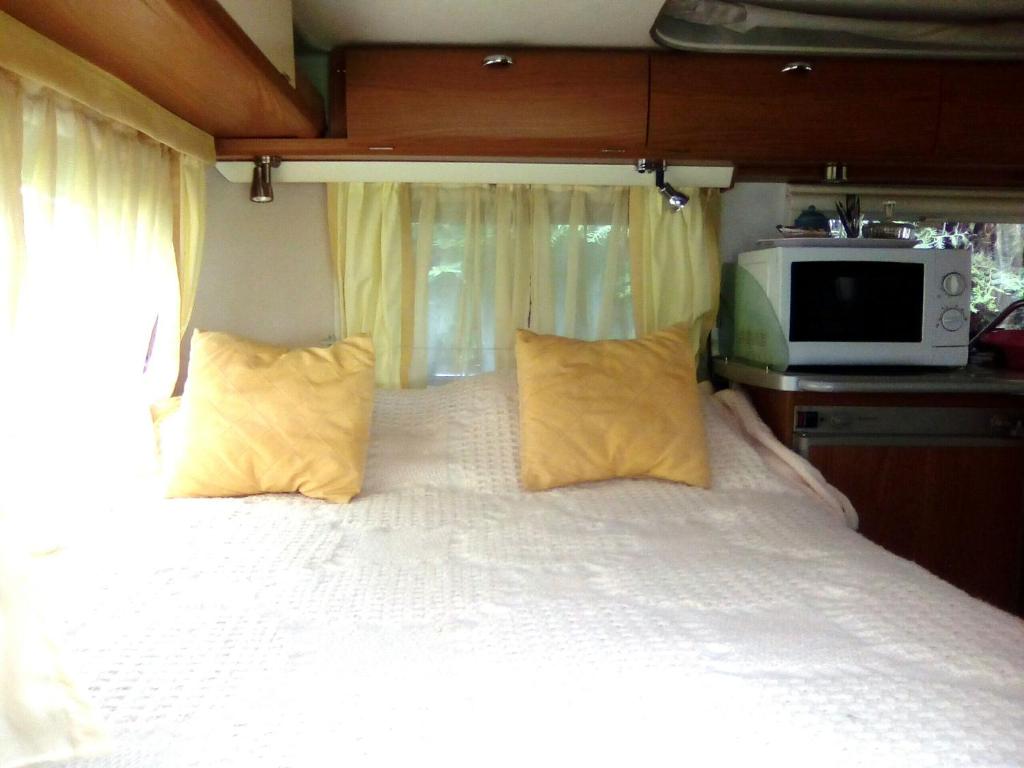 a bedroom with a bed with yellow pillows and a microwave at Caravane Eriba au Bord de l'Eure in Neuilly