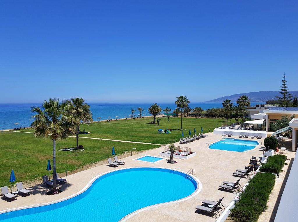 ośrodek z 2 basenami i krzesłami oraz oceanem w obiekcie Natura Beach Hotel And Villas w mieście Polis Chrysochous