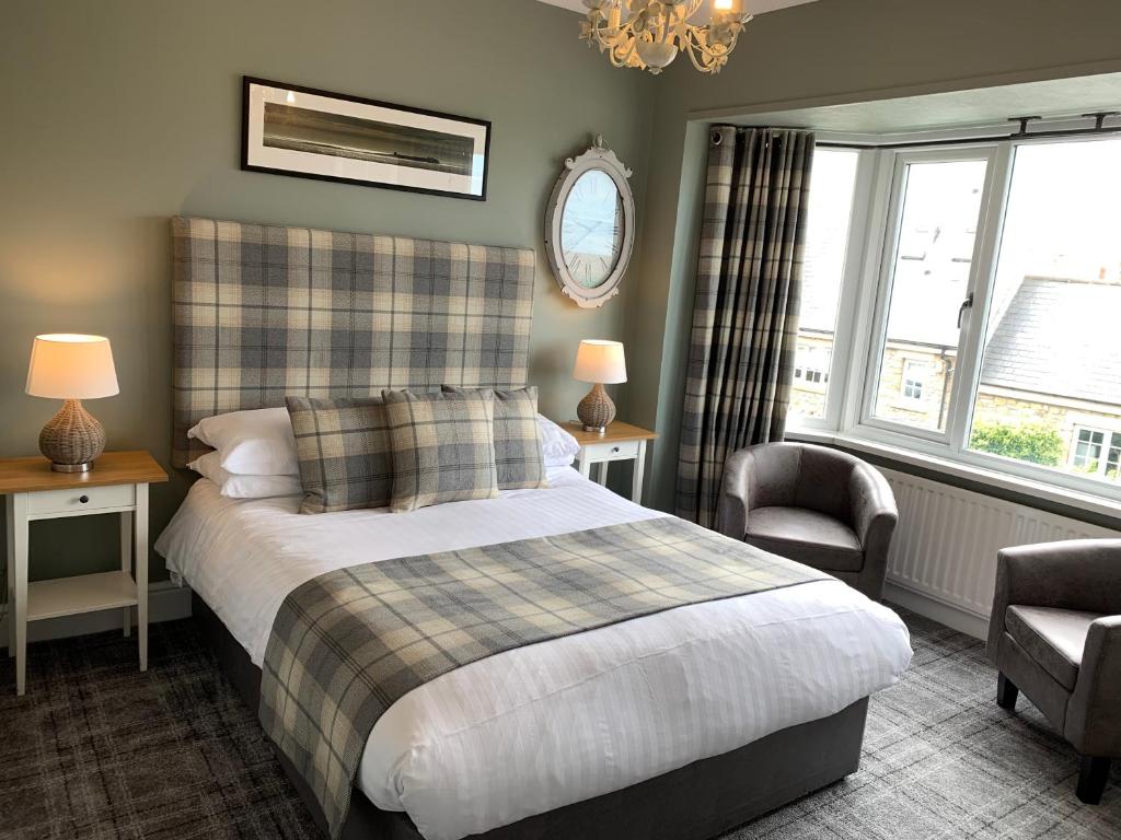 a bedroom with a bed and a chair and windows at The Sunningdale in Bamburgh